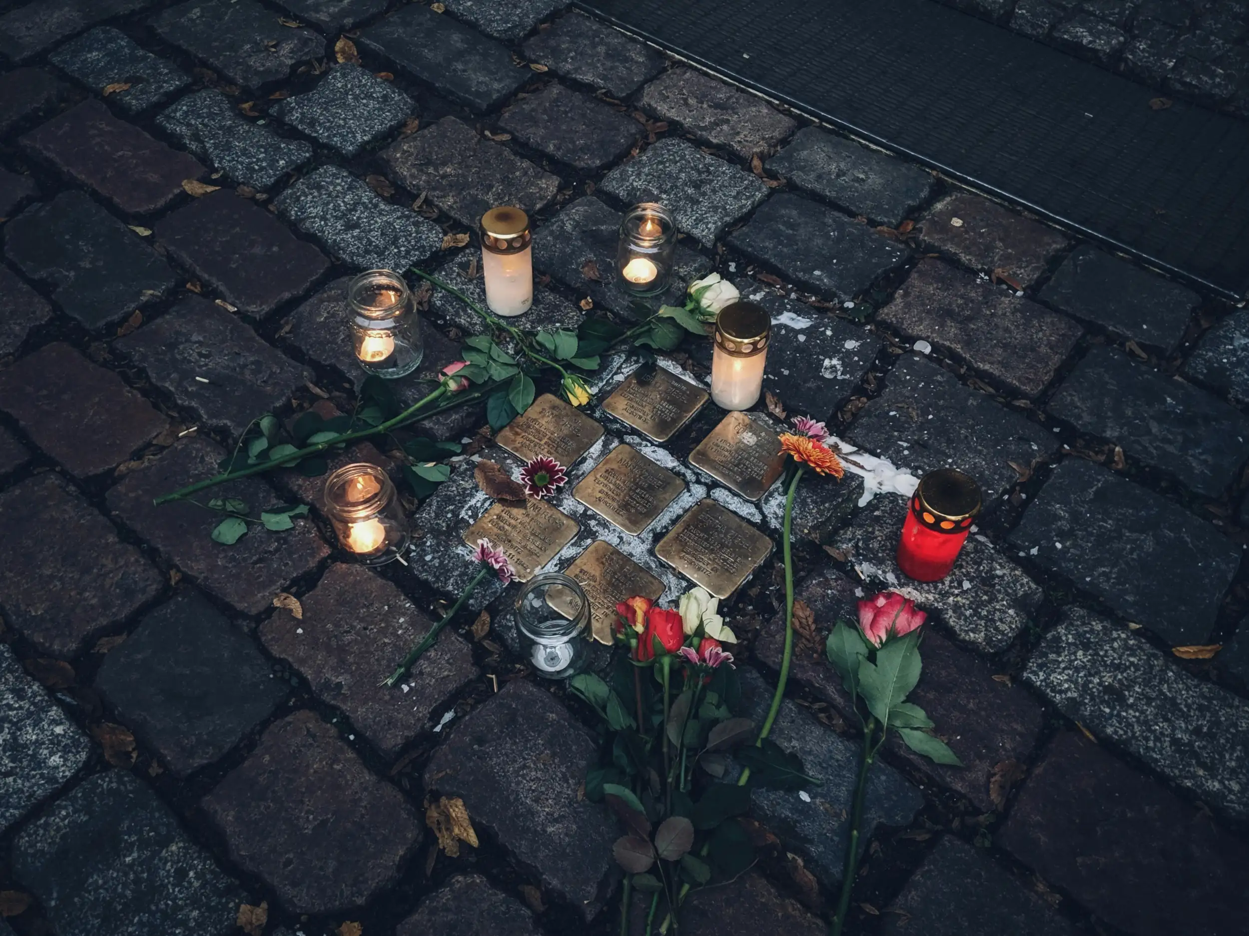 Grabkerzen und Blumen um eine Gruppe Stolpersteine